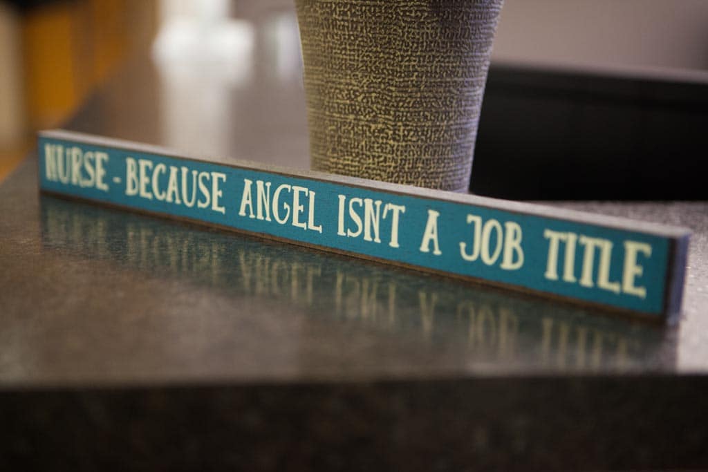 Picture of a small wooden sign on top of the reception counter that reads "Nurse-because angel isn't a job title."