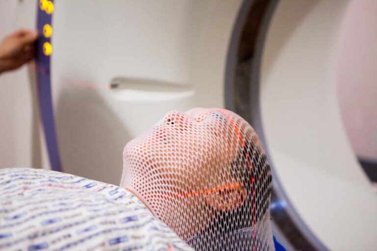 Man is prepared for radiation treatment; he is laying on the bed wearing a mesh radiation mask.